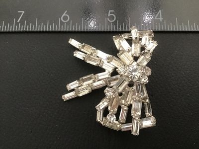 Sale Photo Thumbnail #56: A vintage silver-tone costume jewelry brooch in a dimensional bow design, set with baguette and round cut clear rhinestones. Features a pin stem and roll-over safety clasp on the reverse. Measures approximately 2 inches wide by 2 inches long. Good vintage