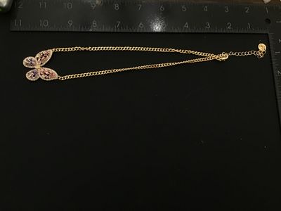 Sale Photo Thumbnail #104: Gold-tone chain necklace featuring a stylized butterfly pendant set with purple, pink, and clear rhinestones. Features a logo hang tag at the clasp extender. Measures approximately 11 inches in total laid-flat length including the pendant. In good pre-own