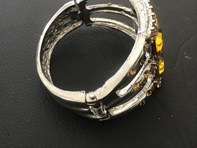 Sale Photo Thumbnail #118: Silver-tone metal hinged cuff bracelet featuring six large square-cut yellow/amber faux crystal central stones bordered by smaller amber-colored rhinestones. Features a spring-hinged closure. Good pre-owned condition with minor finish wear to the reverse.