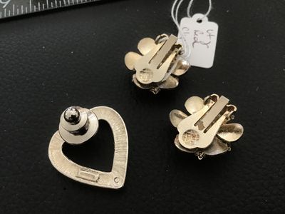 Sale Photo Thumbnail #49: A 3-piece lot of vintage costume jewelry featuring a pair of gold-tone flower clip-on earrings with deep red enamel petals and central faux ruby red rhinestones, alongside a silver-tone open heart lapel pin lined with clear rhinestones and secured with a 