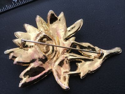 Sale Photo Thumbnail #113: Vintage gold-tone floral motif brooch pin featuring white enamel details and clear rhinestone accents. Shows noticeable surface wear, plating loss, enamel chipping, and age-related patina on the finish. The pin mechanism on the reverse is intact and funct