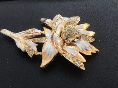 Sale Photo Thumbnail #111: Vintage gold-tone floral motif brooch pin featuring white enamel details and clear rhinestone accents. Shows noticeable surface wear, plating loss, enamel chipping, and age-related patina on the finish. The pin mechanism on the reverse is intact and funct