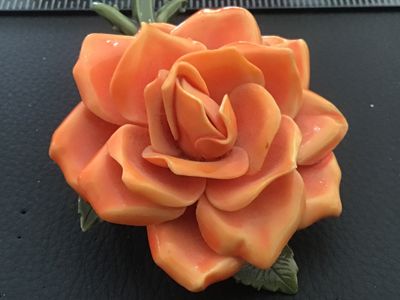 Sale Photo Thumbnail #30: Vintage dimensional orange rose brooch crafted from molded celluloid/plastic material with green stem and leaves on the back. Features a safety pin style clasp mechanism attached to the back. Measures approximately 2.5 inches across. Good pre-owned vintag