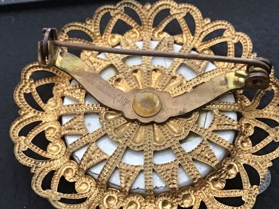 Sale Photo Thumbnail #95: Vintage round filigree brooch pin featuring a central cabochon decorated with a printed floral flower basket design. The gold-tone brass or alloy frame features ornate openwork filigree hearts and dots. Marked 'WESTERN GERMANY' on the back bar mechanism. 