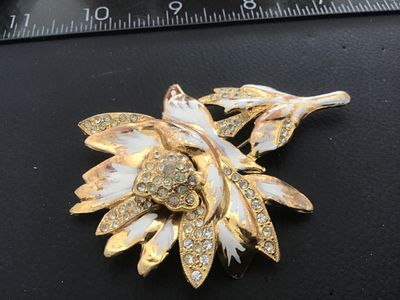 Sale Photo Thumbnail #109: Vintage gold-tone floral motif brooch pin featuring white enamel details and clear rhinestone accents. Shows noticeable surface wear, plating loss, enamel chipping, and age-related patina on the finish. The pin mechanism on the reverse is intact and funct