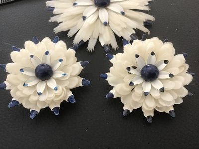 Sale Photo Thumbnail #136: Matching 3-piece vintage jewelry set featuring a large floral brooch pin and two clip-on earrings. Crafted from layered white celluloid petals with painted blue tips and a dark blue center cabochon accent. Brooch measures approximately 3.5 inches across. 