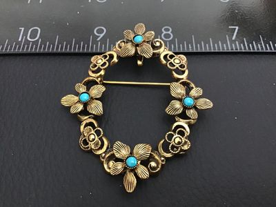 Sale Photo Thumbnail #162: Vintage gold-tone openwork wreath brooch featuring embossed flowers accented with round turquoise-colored cabochons. Includes a rollover C-clasp pin back and an integrated pendant bail on the reverse for dual wear as a brooch or pendant. Measures approxim