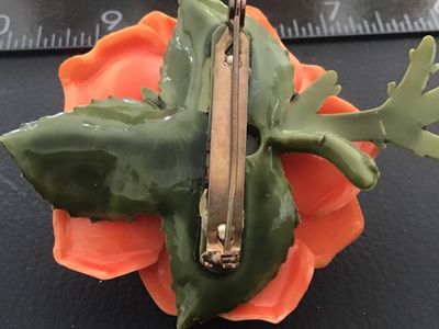 Sale Photo Thumbnail #31: Vintage dimensional orange rose brooch crafted from molded celluloid/plastic material with green stem and leaves on the back. Features a safety pin style clasp mechanism attached to the back. Measures approximately 2.5 inches across. Good pre-owned vintag