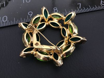 Sale Photo Thumbnail #210: A vintage gold-tone wreath brooch set with alternating emerald green and peridot lime green navette/marquise cut rhinestones in prong settings. Features a rollover safety clasp mechanism. Measures approximately 2 inches in diameter. Good vintage condition