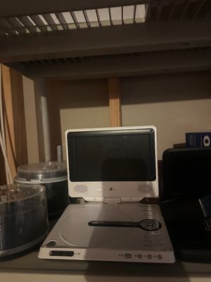 Sale Photo Thumbnail #31: Silver Zenith portable DVD player sitting open on a shelf, displayed alongside plastic spindle cases of blank or burned discs.