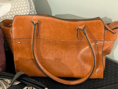 Cognac brown faux leather shoulder handbag featuring double top handles, a front slip pocket, and black edge painting.