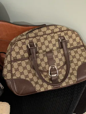 Gucci GG monogram canvas handbag with brown leather trim, rolled handles, and a front buckled pocket detail.