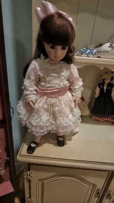 Vintage porcelain collector doll wearing a white lace dress with a pink sash and matching hair bow.