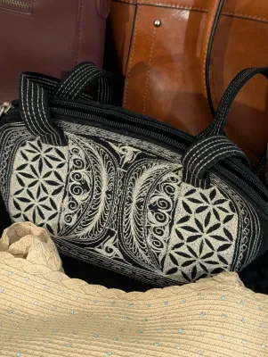 Black embroidered fabric barrel bag with geometric and scroll designs, displayed alongside other purses.