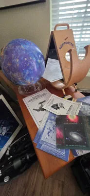 Sale Photo Thumbnail #99: Wooden Sunspotter solar telescope set on a tabletop alongside a celestial globe and astronomical instruction manuals.