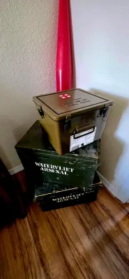 Sale Photo Thumbnail #51: Military surplus olive drab general purpose first aid kit box resting on stacked Watervliet Arsenal wooden ammo crates, with a red inert ordnance cone in the background.