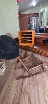 Sale Photo Thumbnail #82: Rustic wooden child's rocking chair with woven seat, alongside a wooden desk organizer and a black felt hat.