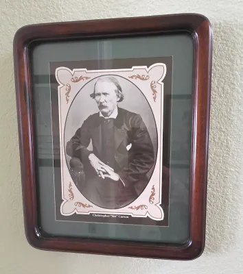 Sale Photo Thumbnail #73: Framed portrait print of Christopher "Kit" Carson housed in a dark wooden shadowbox-style frame with rounded corners.