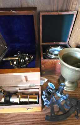 Sale Photo Thumbnail #14: Collection of nautical instruments including brass sextants, a gimbaled box compass, and a brass spyglass telescope in wooden display cases.