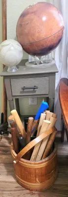 Sale Photo Thumbnail #62: A collection of wooden handles and tools in a rustic wooden bucket, positioned next to a gray nightstand displaying two MOVA globe models.