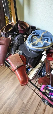 Sale Photo Thumbnail #64: Collection of vintage leather gun holsters, thick leather belts, and a Civil War-style blue officer's kepi hat displayed on a wire rack.