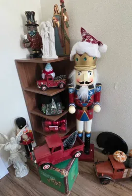Sale Photo Thumbnail #46: Collection of Christmas decorations including large nutcrackers, red vintage-style truck models, religious figurines, and ornaments displayed on and around a wooden shelf unit.