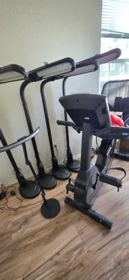 Sale Photo Thumbnail #45: Collection of black modern floor lamps, including gooseneck task lights and an LED arc lamp, alongside a stationary exercise bike.