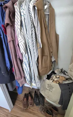 Sale Photo Thumbnail #70: Selection of vintage men's clothing hanging in a closet, including striped long-sleeve shirts, a tan vest, shoes, and a canvas Federal Reserve Bank bag.