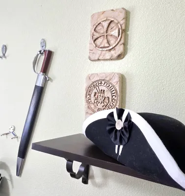 Sale Photo Thumbnail #69: Collection of historical replica decor, including a military-style tricorn hat with cockade, a sheathed saber, and two stone-style Templar seal wall plaques.