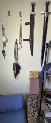 Sale Photo Thumbnail #65: Collection of medieval-style replica swords and scabbards mounted on a wall alongside beaded jewelry, small pouches, and decorative storage boxes below.