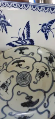 Sale Photo Thumbnail #90: Pair of blue and white Asian ceramic items featuring hand-painted designs, including a small dish with a central spiral and scroll pattern, set against a larger plate decorated with butterflies.