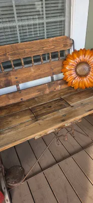 Sale Photo Thumbnail #35: Rustic wooden outdoor bench with turned spindles and metal base, styled with a bright orange metal sunflower wall decor piece.
