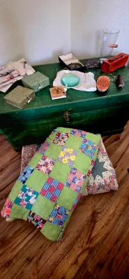 Sale Photo Thumbnail #52: Vintage handmade patch quilts stacked in front of a green painted wooden trunk topped with small trinkets, fabric boxes, and a magnifying lens.