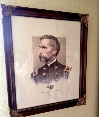 Sale Photo Thumbnail #58: Framed historical portrait print of Colonel Joshua Lawrence Chamberlain of the Twentieth Maine, featuring a dark wooden frame with ornate gilt corner accents.