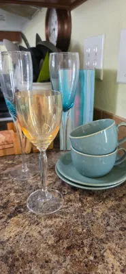 Sale Photo Thumbnail #91: Collection of drinkware featuring an amber iridescent wine glass, two champagne flutes with blue accents, and a pair of teal ceramic teacups with saucers.