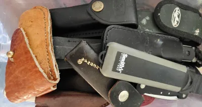 Sale Photo Thumbnail #8: Assortment of pocket knife sheaths and sharpening tools, including leather Buck Knives sheaths, a Herman sheath, and a Smith's knife sharpener.
