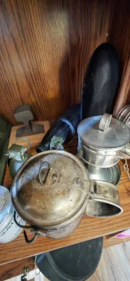 Sale Photo Thumbnail #21: Collection of vintage military gear and memorabilia, including a metal mess kit pot, inert grenade, shell casing replica, and railroad track section paperweight.