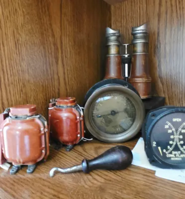 Sale Photo Thumbnail #11: Collection of vintage nautical and aviation instruments, including a cowl flaps gauge, brass round gauge, leather-bound opera glasses, reddish electrical components, and a wooden-handled tool.