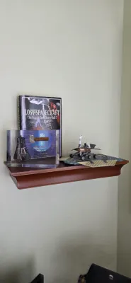 Sale Photo Thumbnail #101: Space exploration memorabilia display featuring a copy of 'Lost Spacecraft: The Search for Liberty Bell 7', an acrylic space capsule commemorative block, and a Mars rover model on a wall-mounted wooden shelf.