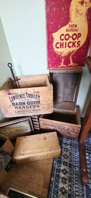 Sale Photo Thumbnail #10: Collection of vintage wooden advertising crates, including Lawrence Trolley Barn Door Hangers and Hercules Powder, displayed beneath a Farm Bureau Co-Op Chicks sign.