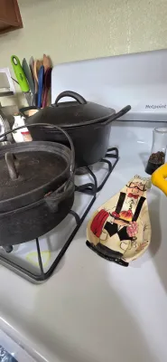 Sale Photo Thumbnail #74: Two black cast iron Dutch ovens with lids sitting on a stovetop, alongside a novelty chef-shaped ceramic spoon rest.