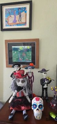Sale Photo Thumbnail #106: Collection of Day of the Dead figurines and art, including Catrina statues, a mariachi musician, a decorated sugar skull, a rag doll, and framed artwork.