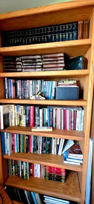 Sale Photo Thumbnail #54: Tall oak wood bookcase filled with various hardcover and paperback books, including matched leather-bound encyclopedia and history sets.