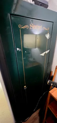 Sale Photo Thumbnail #22: Green Sentinel gun cabinet or metal safe with gold lettering, featuring some surface wear and sticker residue on the front door.