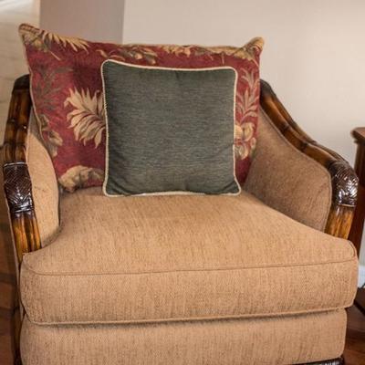 Two matching oversized upholstered chairs by Cindy Crawford with contrasting pillows, carved arms and rich wood accents.