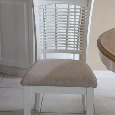 Kitchen dining set with driftwood-finish top and four white chairs with neutrally upholstered seat cushions.  Hillsdale 48" round.