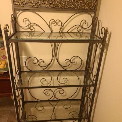 Pretty metal bakers rack with four glass shelves. Leaf and vine design flows across the top piece. The shelf is painted metallic grey and...