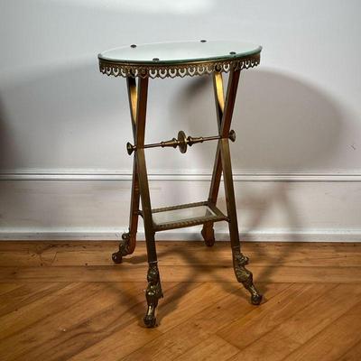 BRASS SIDE TABLE  |  Having an oval mirrored top, with a medial glass shelf - l. 18 1/2 x w. 11 3/4 x h. 29 3/4 in.