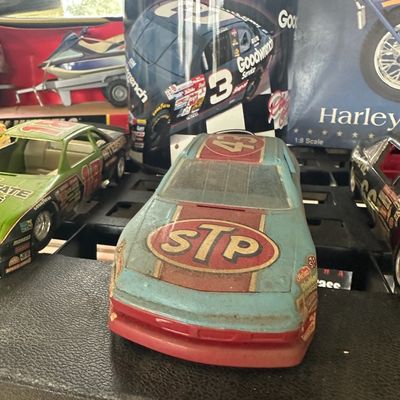 Vintage Richard Petty STP #43 NASCAR race car coin bank displaying surface dust and wear, flanked by other die-cast race car collectibles.