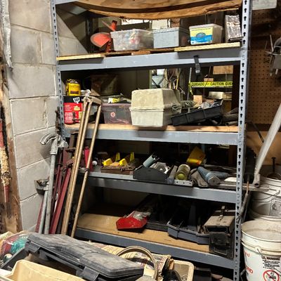Heavy-duty steel industrial shelving unit loaded with various workshop supplies, toolboxes, hardware, and equipment.